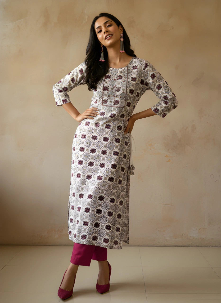 Woman wearing a patterned kurta with pink pants against a beige background